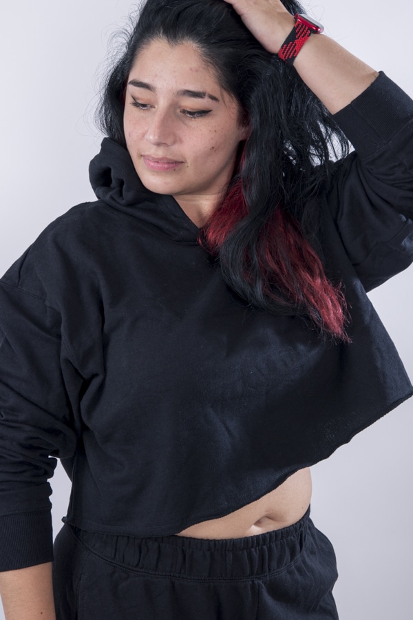 Femme vue de face portant un sweatshirt court en french terry de couleur noir avec capuche.