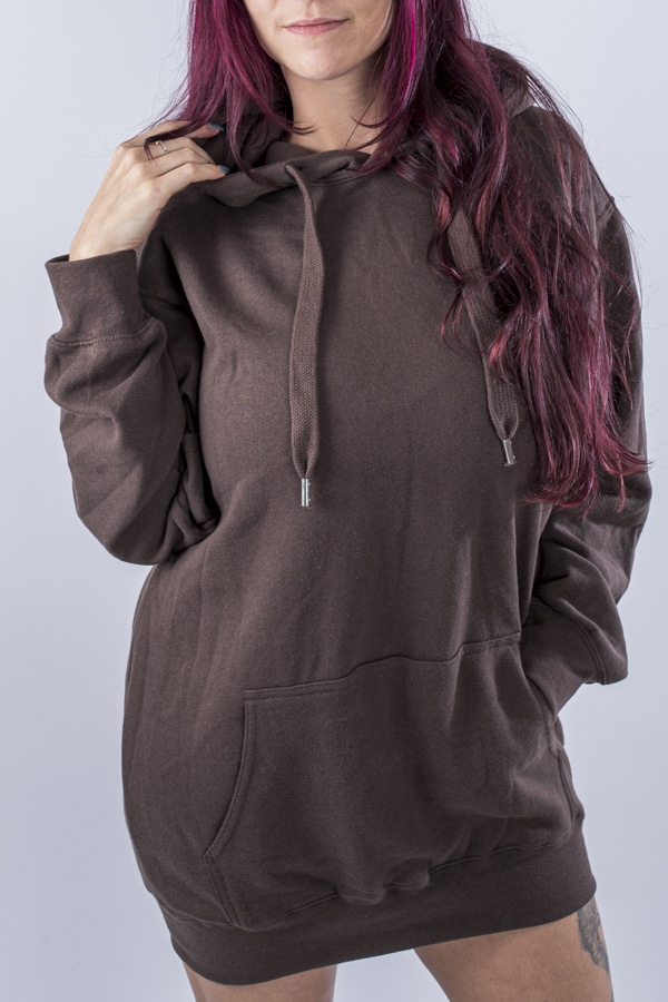 Femme vue de face portant un sweatshirt oversize en fleece de couleur brun avec capuche et poche kangourou.