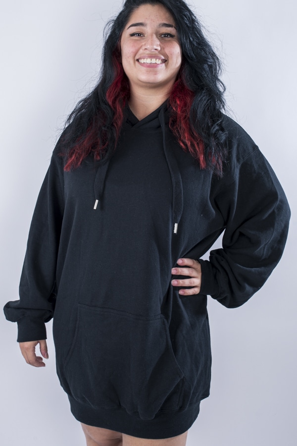 Femme vue de face portant un sweatshirt oversize en fleece de couleur noir avec capuche et poche kangourou.