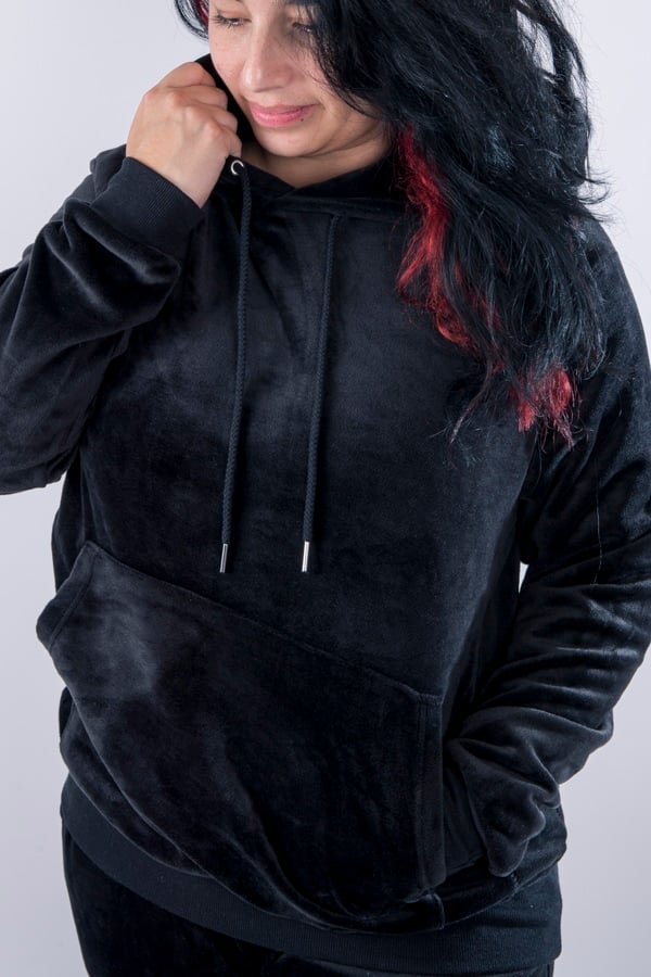 Femme vue de face portant un sweatshirt noir en velours avec capuche et poche kangourou.