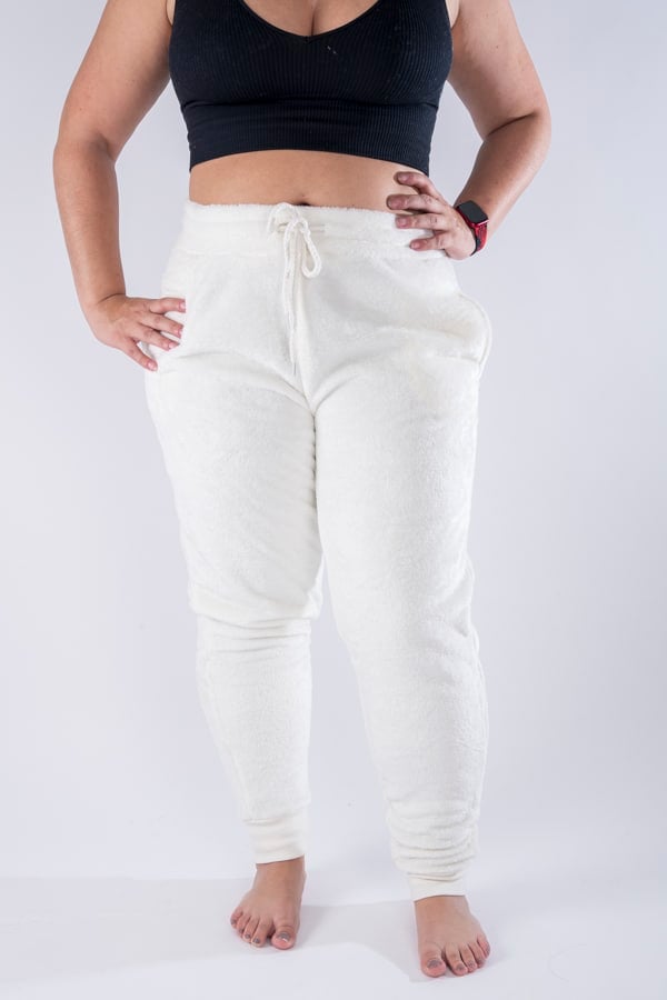 Femme vue de face portant un jogging en peluche de couleur crème. Avec des poches et un cordon ajustable.