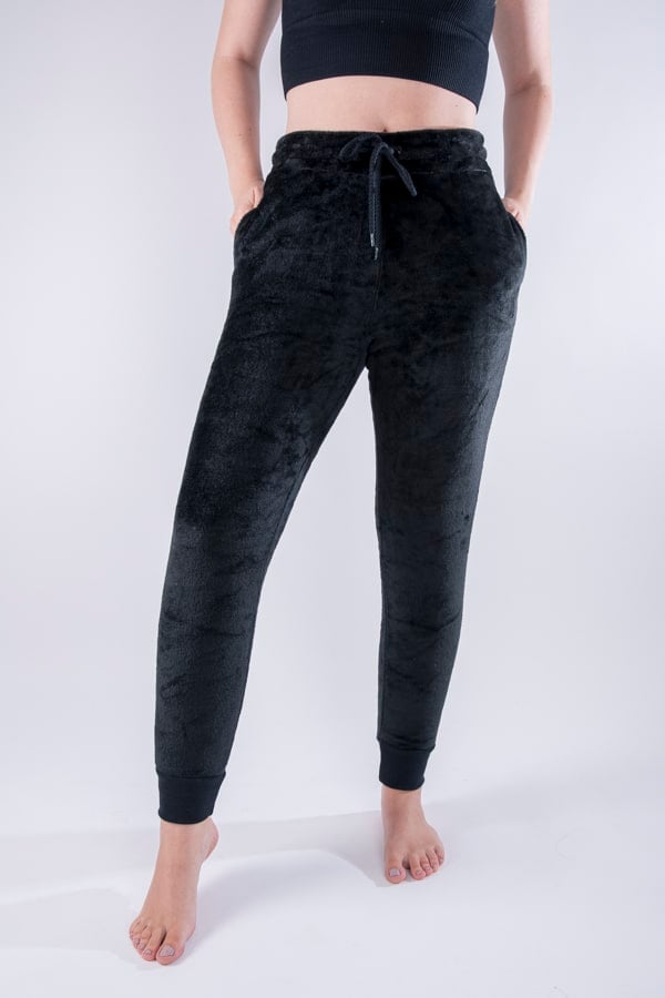 Femme vue de face portant un jogging en peluche de couleur noir. Avec des poches et un cordon ajustable.
