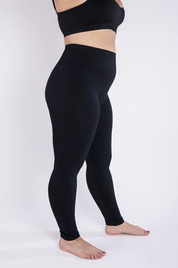 Femme vue de profil qui porte un legging noir en taille unique. Coupe seamless
