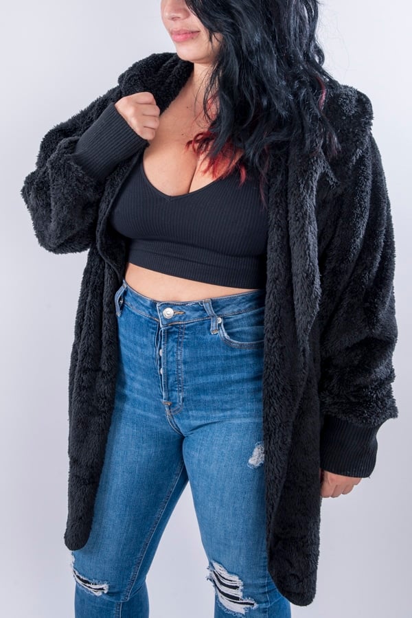 Femme vue de face portant une veste en peluche de couleur noire avec capuche, la veste est de taille unique et offre une coupe ample.