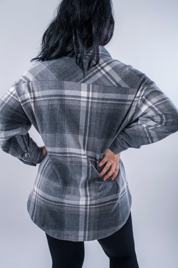 Femme vue de dos portant une veste en plaid de couleur grise avec des poches avants et latérales. Fermeture par boutons à l'avant.