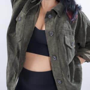 Femme vue de face portant une veste en velours côtelé de couleur olive. Avec une fermeture par boutons à l'avant et des poches latérales. Cette veste offre une coupe ample et décontractée.